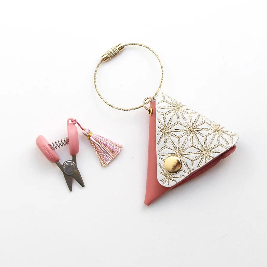 A pink and white keychain with a tassel and a pair of scissors is shown on a white background.