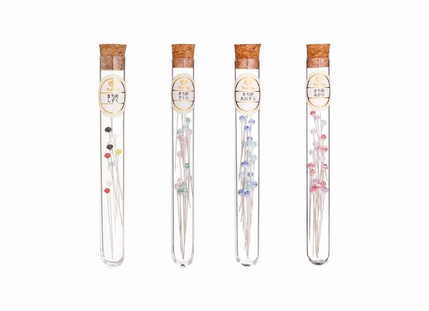 Four glass tubes containing different colored needles, each with a cork stopper.