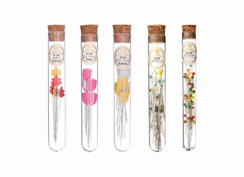 five glass tubes containing different colored needles, each with a cork stopper.