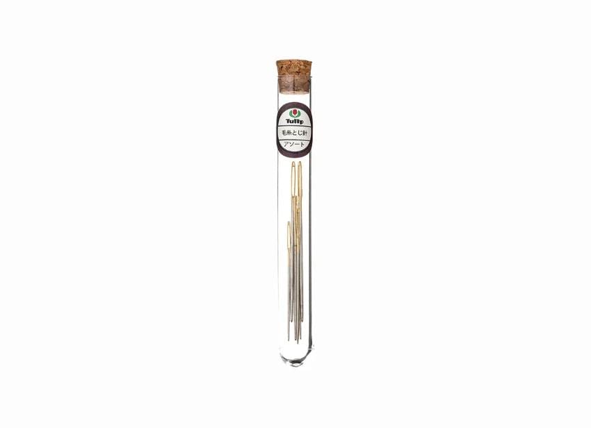 A clear glass tube containing a collection of gold crochet hooks.
