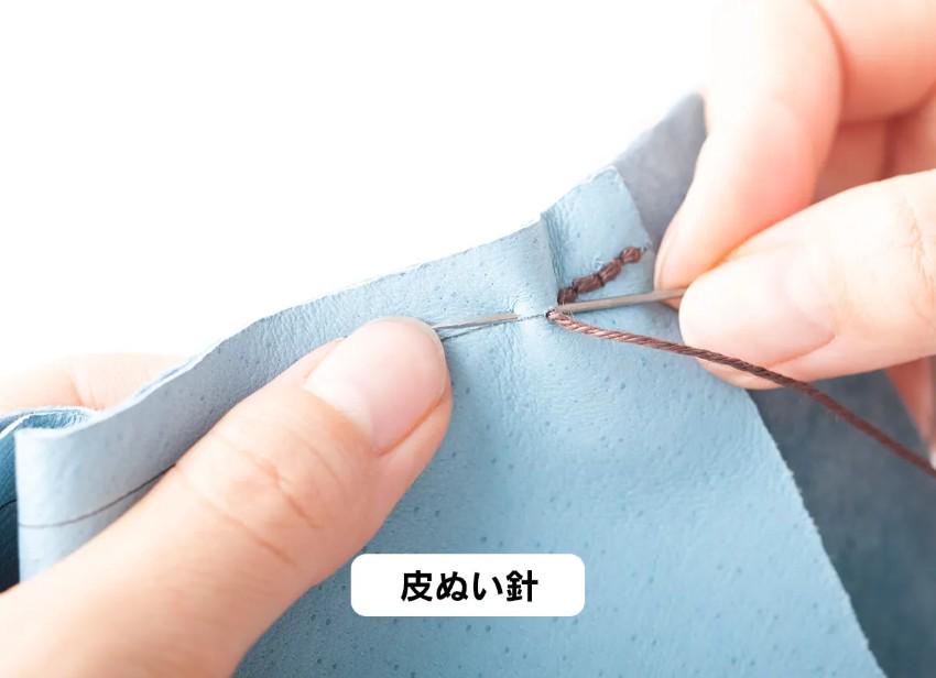 A person's hands are shown carefully stitching a piece of fabric with a needle and thread.