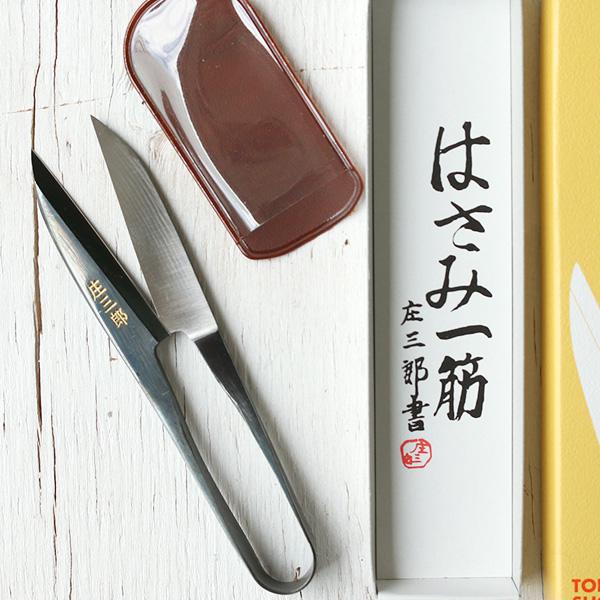 a pair of scissors, a red object, and a white box with Japanese text on it, all placed on a white surface.