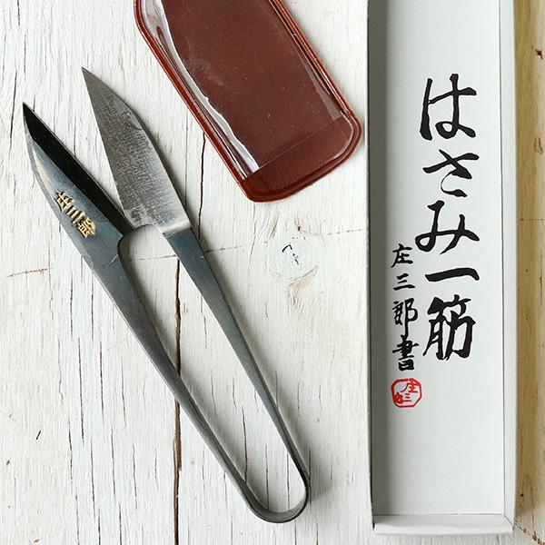 a pair of scissors, a red container, and a white box with Japanese text on it, all placed on a white wooden surface.