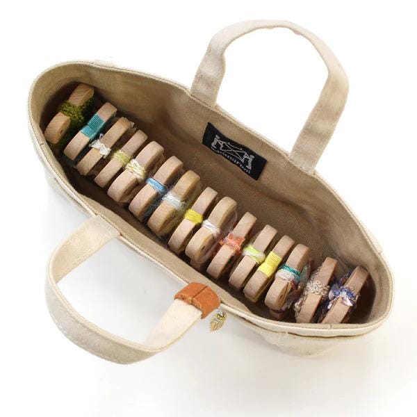 A beige tote bag with a handle, containing a row of colorful wooden objects tied together with string.