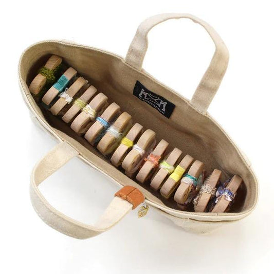 A beige tote bag with a handle, containing a row of colorful wooden objects tied together with string.