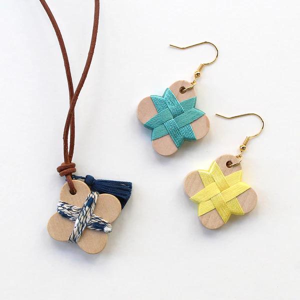 a necklace with a brown leather cord and a pair of earrings made from wood and adorned with colorful ribbons.