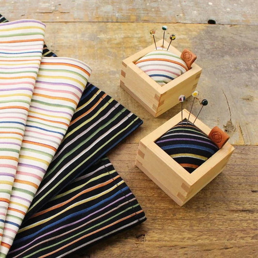 a wooden box with two colorful fabric squares and two small wooden boxes with pins placed inside them, all resting on a wooden surface.