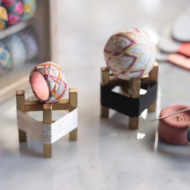 two small, colorful balls placed on wooden stands, with a pink button and a spool of thread visible in the background.