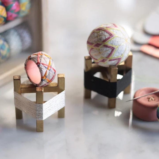 two small, colorful balls placed on wooden stands, with a pink button and a spool of thread visible in the background.