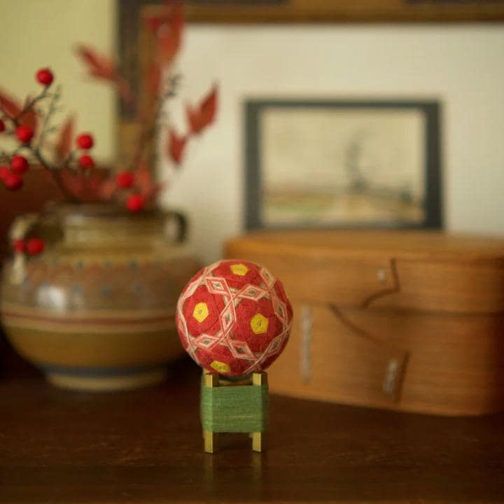 a wooden table with a red and yellow ball on a green stand, a vase with red berries, and a wooden box in the background.