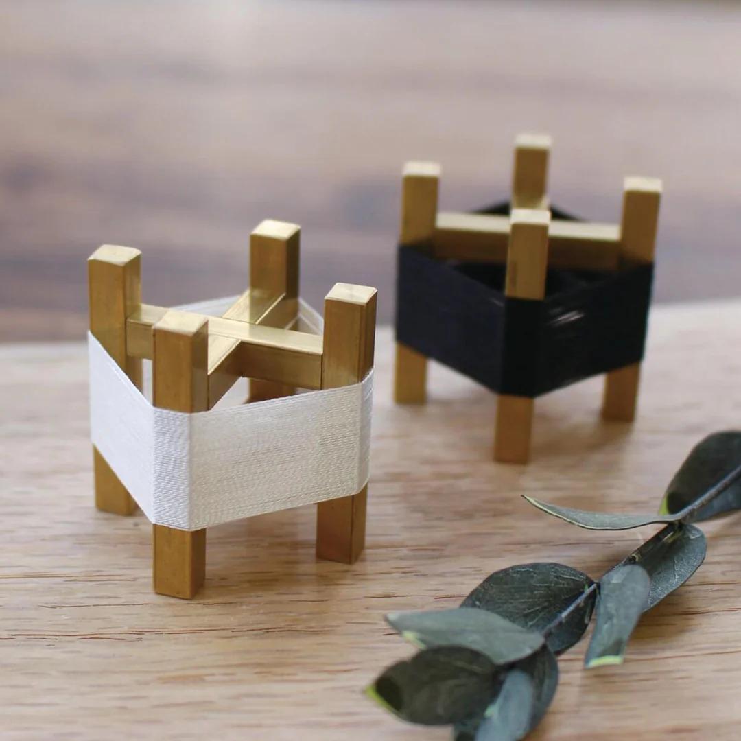 two small wooden stands, one with a white cloth and the other with a black cloth, placed on a wooden surface alongside some green leaves.
