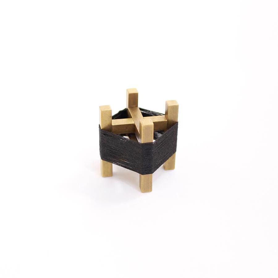 A small, geometric sculpture made of wooden sticks and a black fabric or material, set against a plain white background.