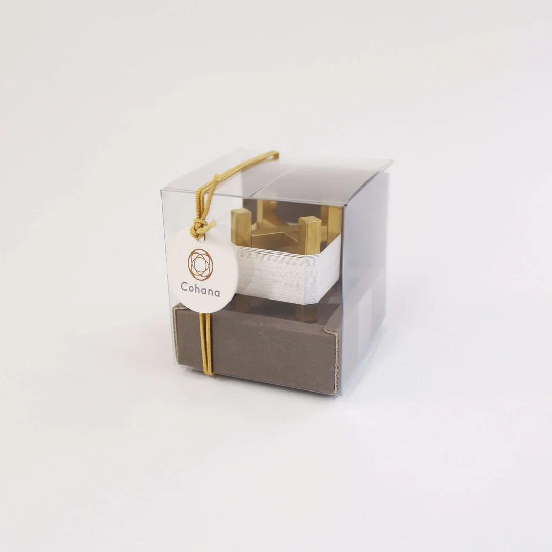 A clear plastic box with a gold ribbon and a white circular tag that says "Cohana" attached to it.