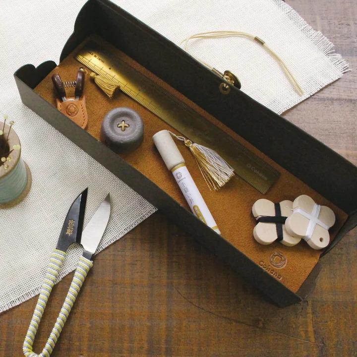 A black box containing various sewing and crafting tools, including scissors, a ruler, and other small items, placed on a wooden surface.