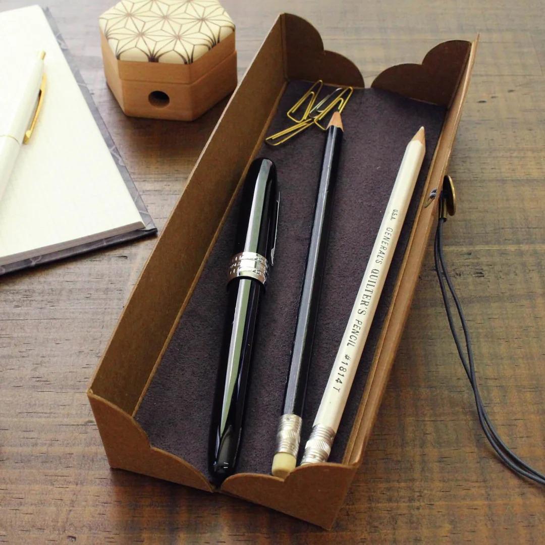 A wooden desk with a brown box, a pen, a pencil, and a stapler.
