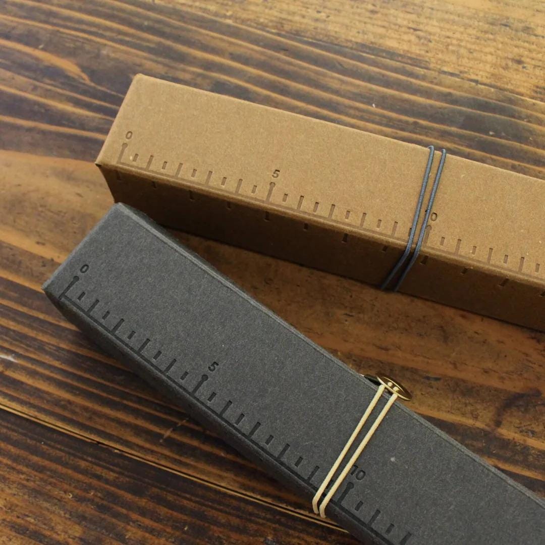 Two rectangular boxes with measurement markings on them, one brown and one gray, tied together with rubber bands.