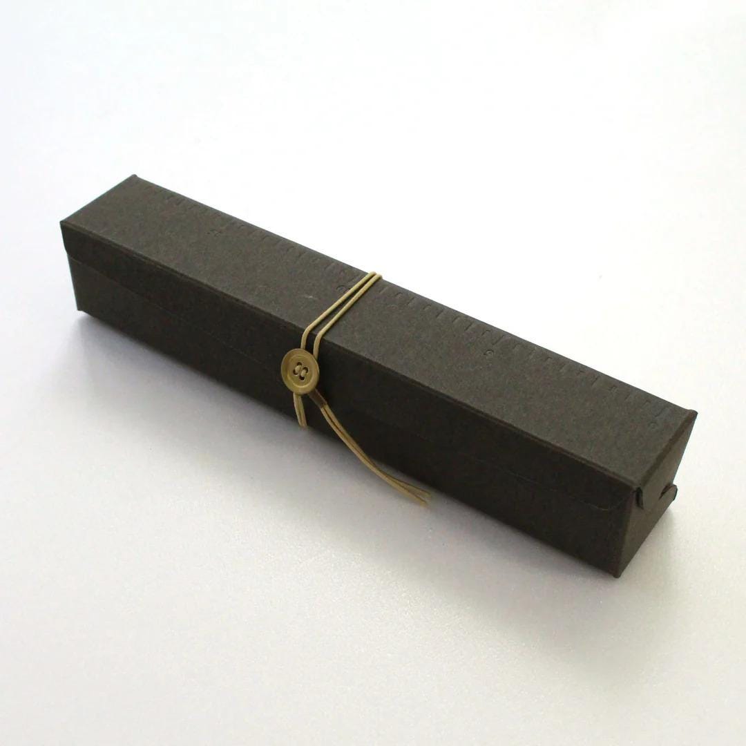 A black rectangular box with a gold button and ribbon tied around it.