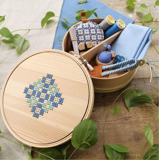 A wooden box with a lid, containing various sewing and crafting supplies, including a cross-stitch design, a needle, thread, and other tools.