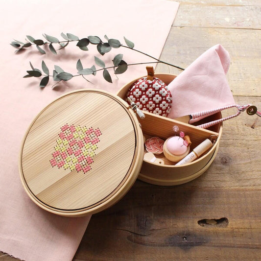 A wooden container with a lid and a compartmentalized design, containing various sewing and crafting supplies, such as a needle, thread, and buttons, placed on a wooden surface.