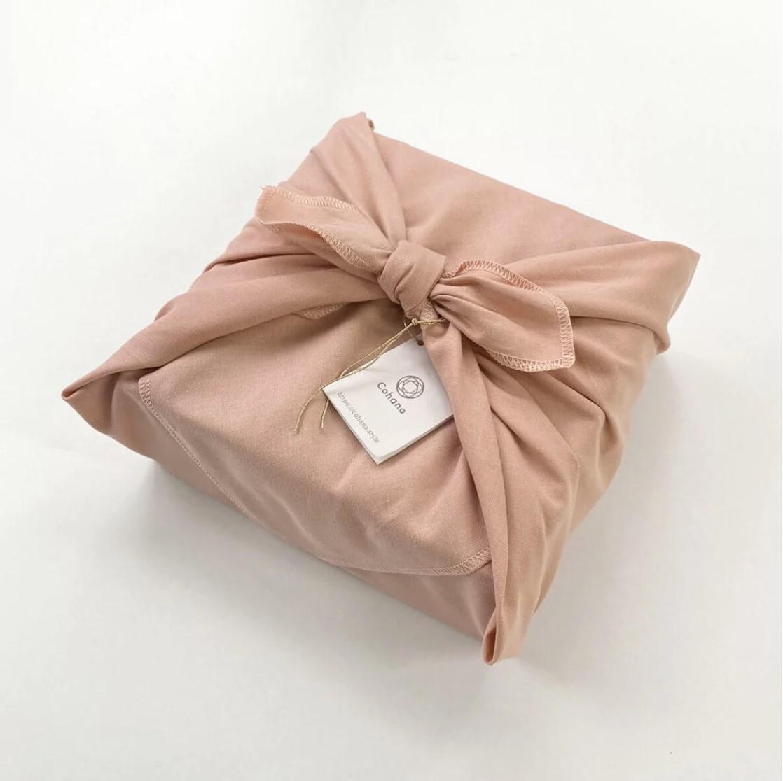 A pink fabric gift box wrapped with a bow and tied with a string, with a small white tag attached.
