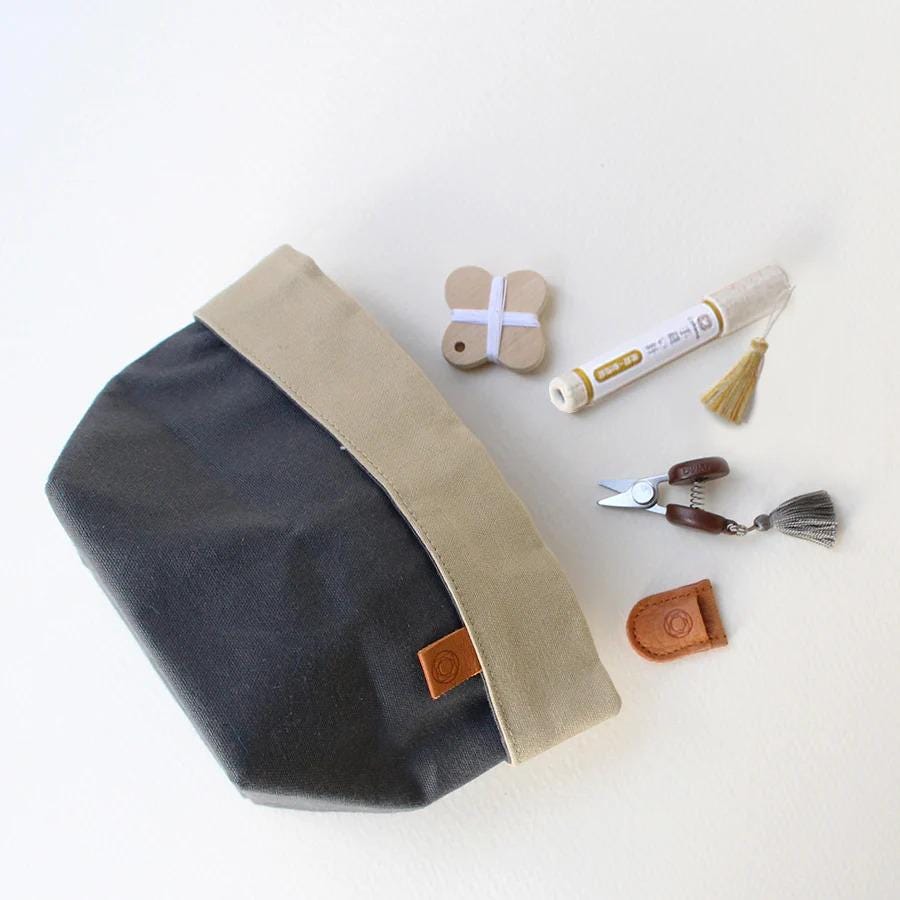 A black and tan tote bag with a tassel, a pair of scissors, and some small items are arranged on a white surface.