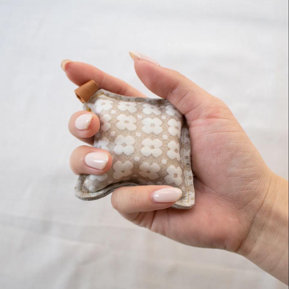 A hand holding a small, beige-colored object with a floral pattern, against a plain white background.