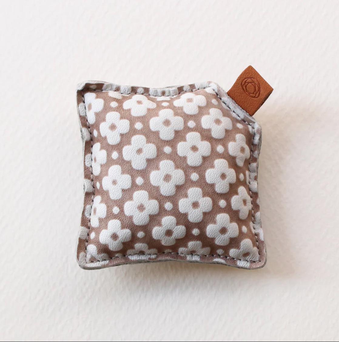 A small, square-shaped cushion with a floral pattern in shades of brown and white.