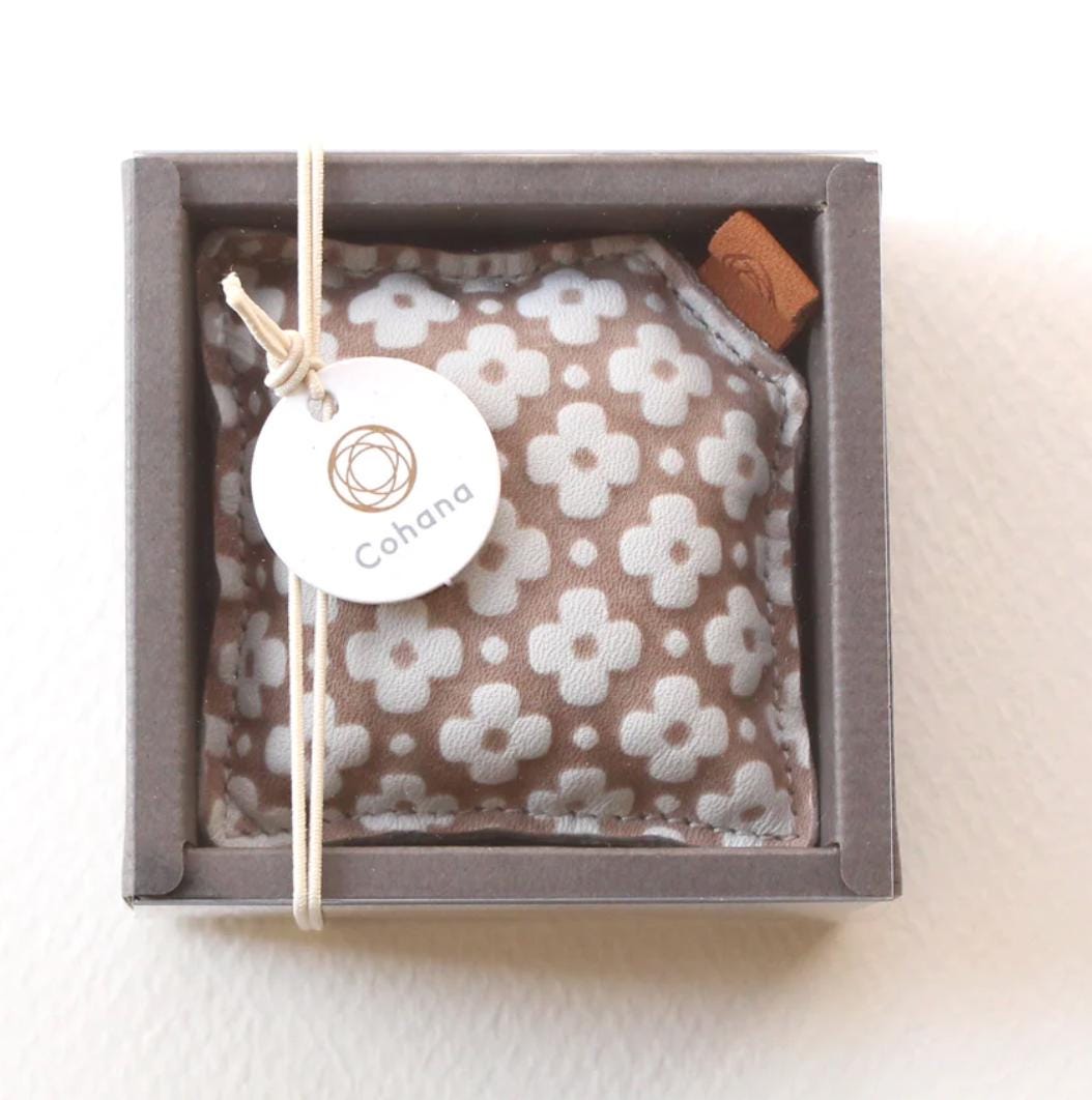 A small square box containing a white and brown floral patterned fabric, with a small brown object attached to the top right corner.