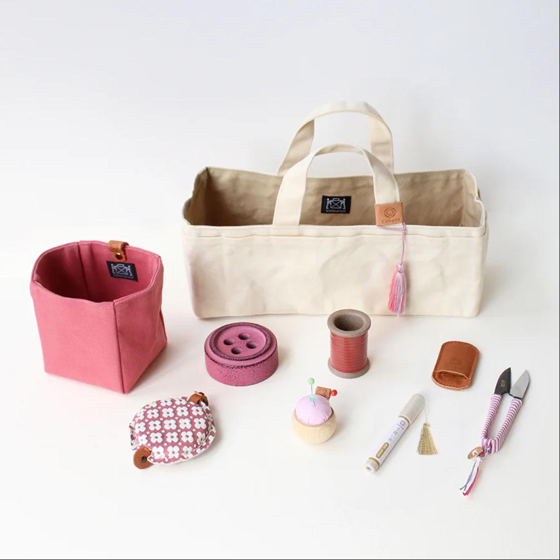 a variety of sewing and crafting supplies, including a beige tote bag, a pink container, a sewing kit, scissors, and other small items.