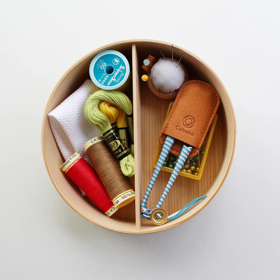 A wooden box containing various sewing and crafting supplies, including spools of thread, needles, and a small stuffed animal.
