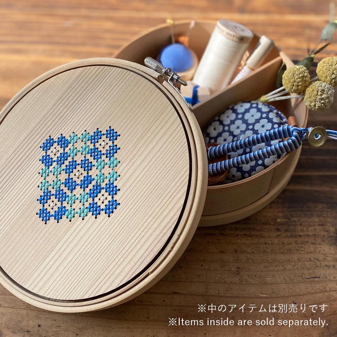 A wooden embroidery hoop with a blue and white floral pattern, along with various sewing and crafting supplies, including a spool of thread and a pair of scissors, all placed on a wooden surface.