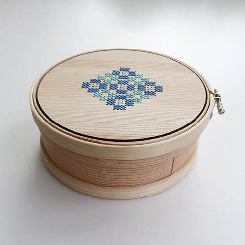 A wooden box with a lid and a lid featuring a blue and white embroidered design.