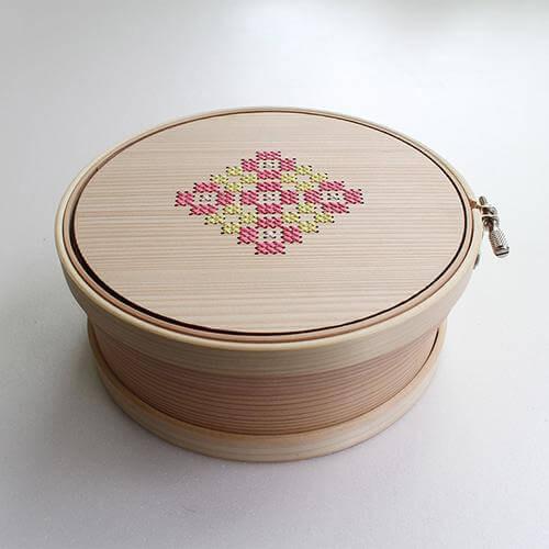 A wooden container with a lid and a decorative cross-stitch design on the lid.