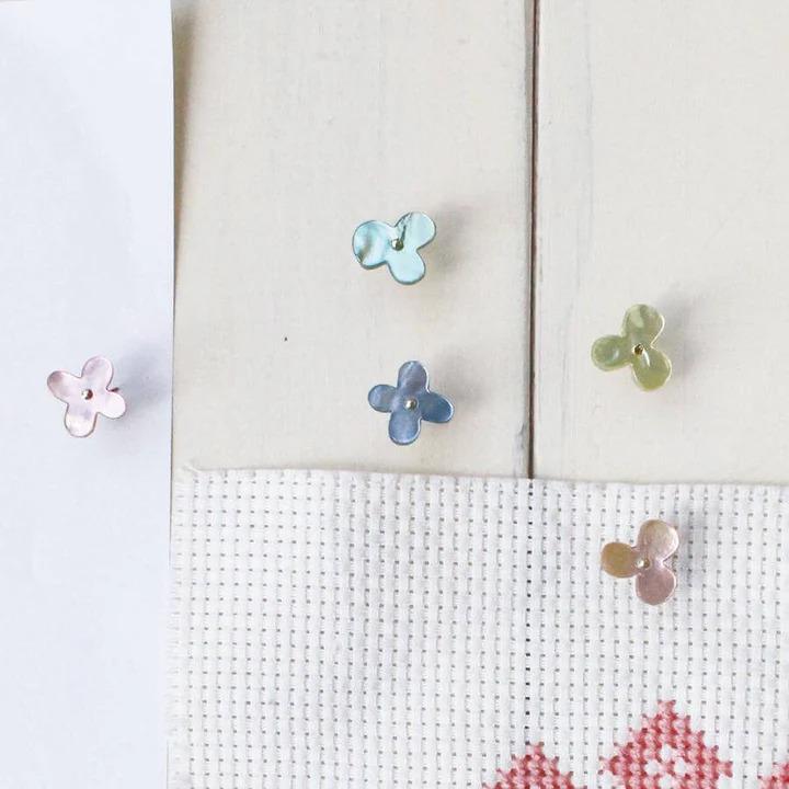 a collection of small, colorful flower-shaped objects, including blue, pink, and green flowers, arranged on a white surface.