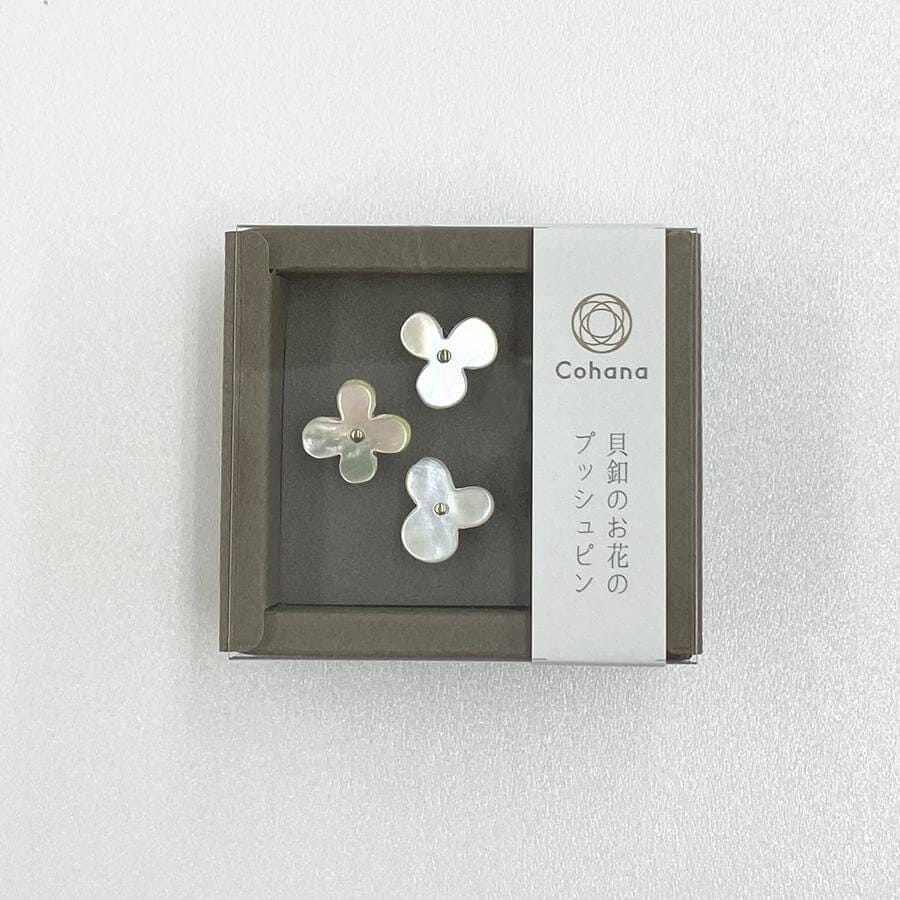 A small square box containing three white flower-shaped pendants, with a label on the side that reads "Cohana" and Japanese text below it.
