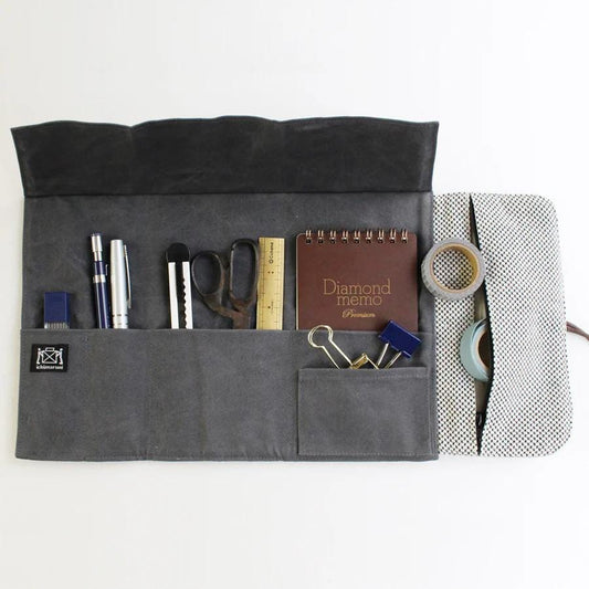 A gray fabric pouch with various office supplies and a notebook inside, including pens, scissors, and a stapler.