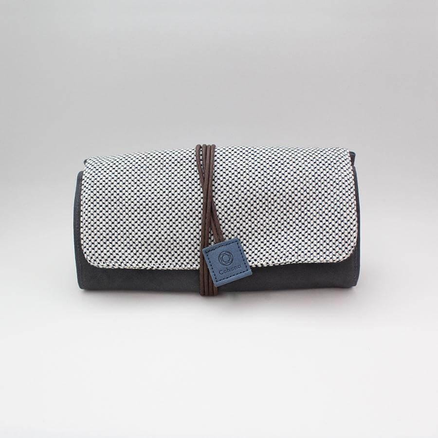 A black and white patterned roll-top bag with a leather strap and a small blue tag attached to it.