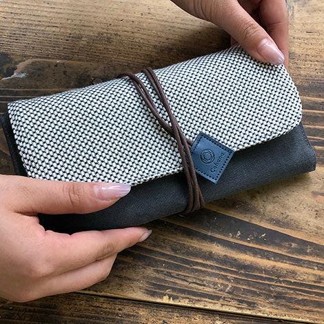 A person's hands holding a black and white woven wallet with a blue logo on it.