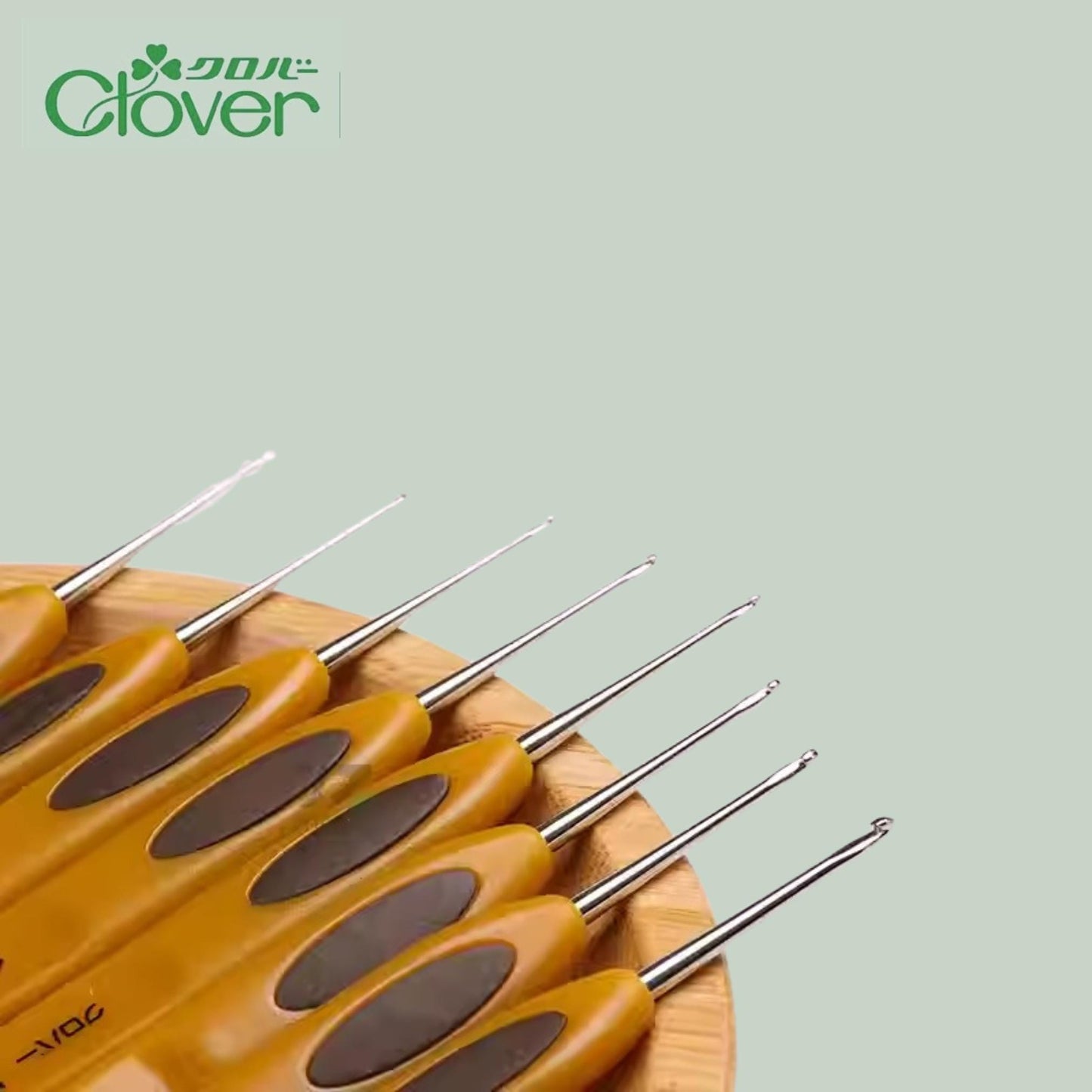 A collection of yellow crochet hooks arranged on a wooden surface, with a green logo in the top left corner.