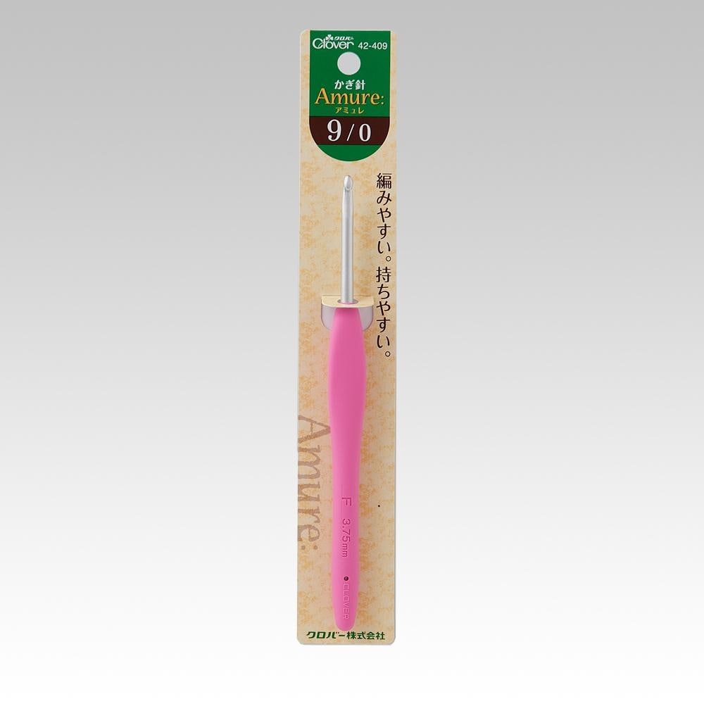 A pink crochet hook with a green and white label on a beige background.