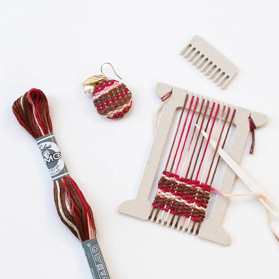 a variety of craft supplies, including a spool of thread, a wooden loom, a comb, and a pair of earrings.