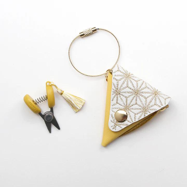 a pair of yellow scissors, a gold-colored keychain, and a small yellow and white triangular coin purse or pouch with a gold-colored button.