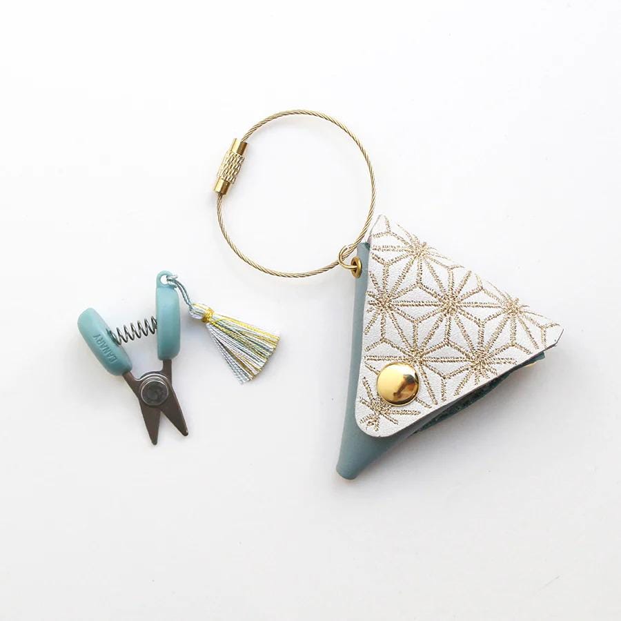 A keychain with a small purse, scissors, and a tassel is shown against a white background.