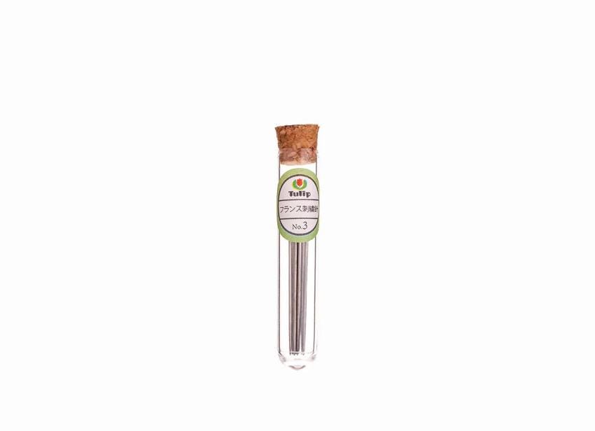 A clear glass tube containing a small amount of a gray substance, with a cork stopper and a label with Japanese text.