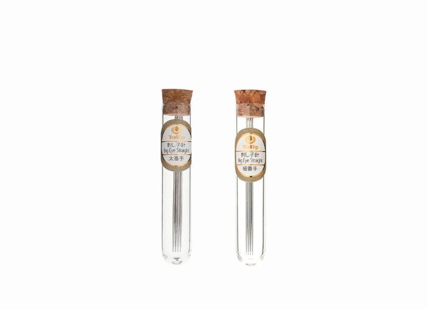 Two glass tubes with metal needles, each with a cork stopper, are shown against a white background.