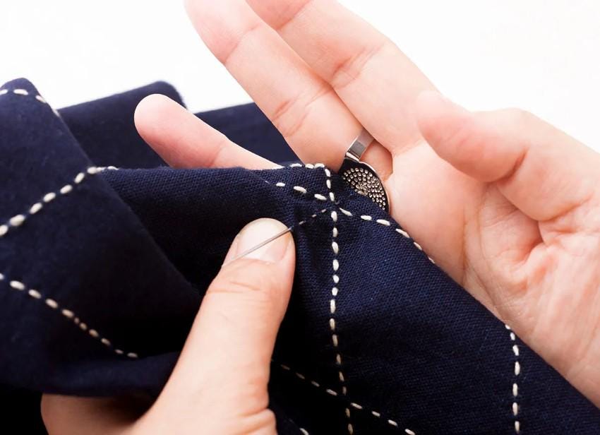 A person's hands are shown carefully stitching a piece of fabric with a needle and thread.
