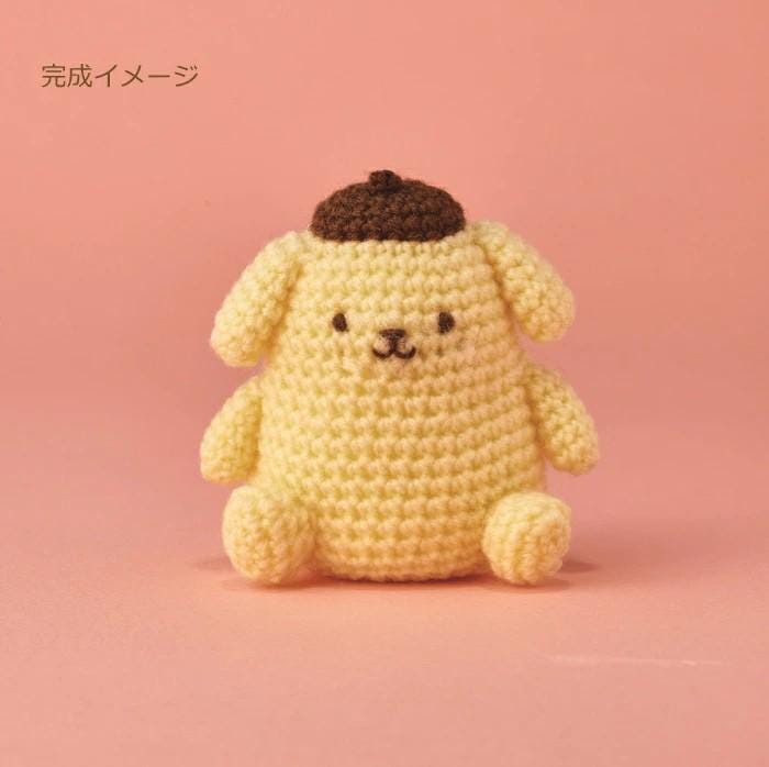 A crocheted toy dog with a brown hat sits on a pink background.