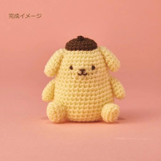 A crocheted toy dog with a brown hat sits on a pink background.