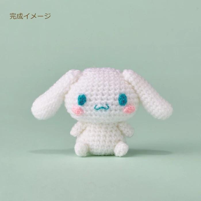 A crocheted white bunny with blue eyes and a pink nose sits on a light green background.