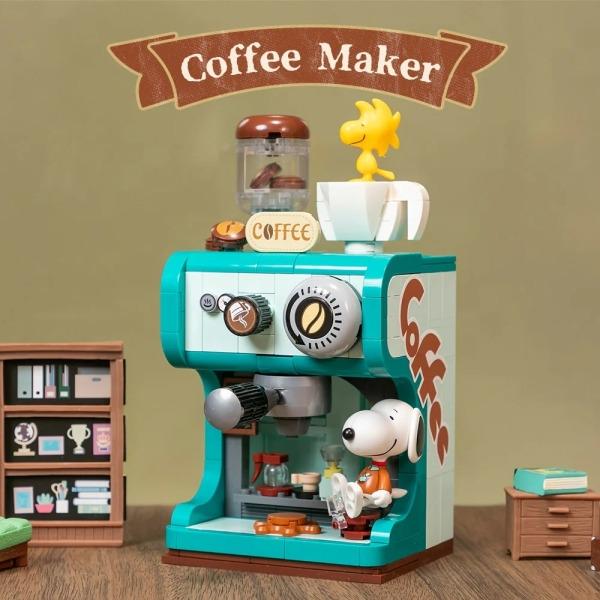 A toy coffee maker with a cartoon Snoopy figurine sitting inside, surrounded by various coffee-related items such as a coffee cup, a coffee grinder, and a bookshelf.